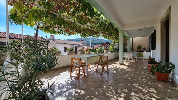 A covered patio with tiled flooring, potted plants, and wooden chairs. - Apartment 2127/39650 (Istria - Rabac), 200m from the beach (Rabac)