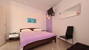 A modern bedroom with a bed, a nightstand, a chair, a TV mounted on the wall, and a bathroom door. - Apartment 2127/39650 (Istria - Rabac), 200m from the beach (Rabac)