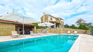 Una piscina amb gandules, un edifici de pedra i un porxo cobert.