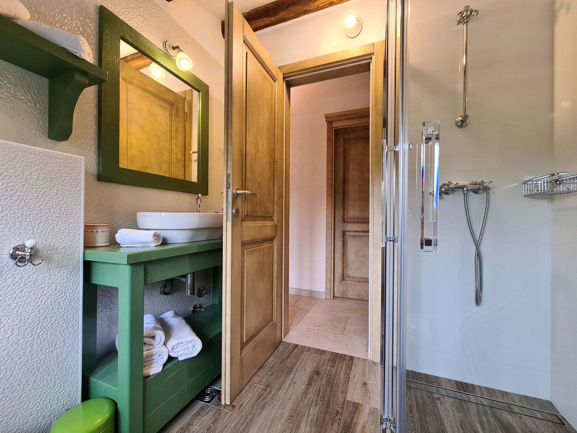 A bathroom with a green vanity, a white sink, and a glass shower enclosure.