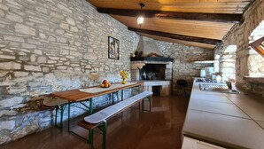 A rustic stone-walled kitchen with a wooden ceiling, a stone fireplace, a wooden table with a bench, and a tiled floor. - House 2134/45311 (Istria - Vidulini), 18000m from the beach (Vidulini)