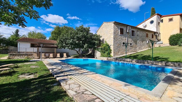 A swimming pool with a stone deck, a stone building with a tiled roof, and a grassy area with trees. - House 2134/45311 (Istria - Vidulini), 18000m from the beach (Vidulini)