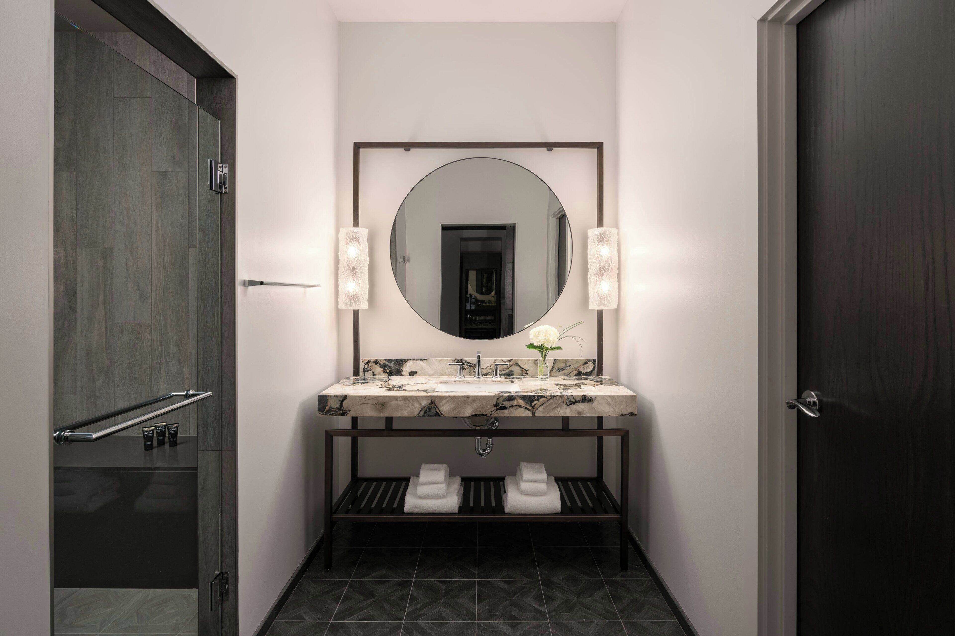 A modern bathroom with a large mirror, a marble sink, and a towel rack.