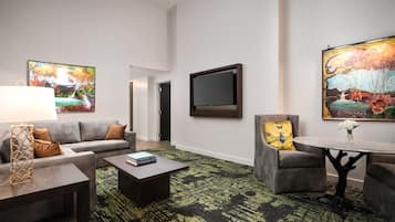 Ein Hotelzimmer mit einer Couch, einem Sessel, einem Couchtisch und einem an der Wand befestigten Fernseher.