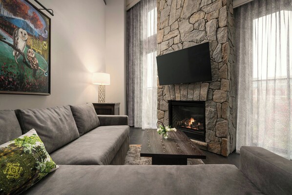 Una sala de estar moderna con chimenea de piedra, un televisor de pantalla plana montado encima y un sofá gris con un cojín decorativo.