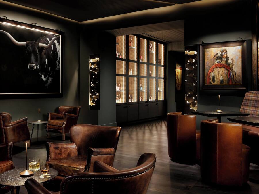 Et dæmpet oplyst loungeområde med læderstole, en bar og billedkunst på væggene.