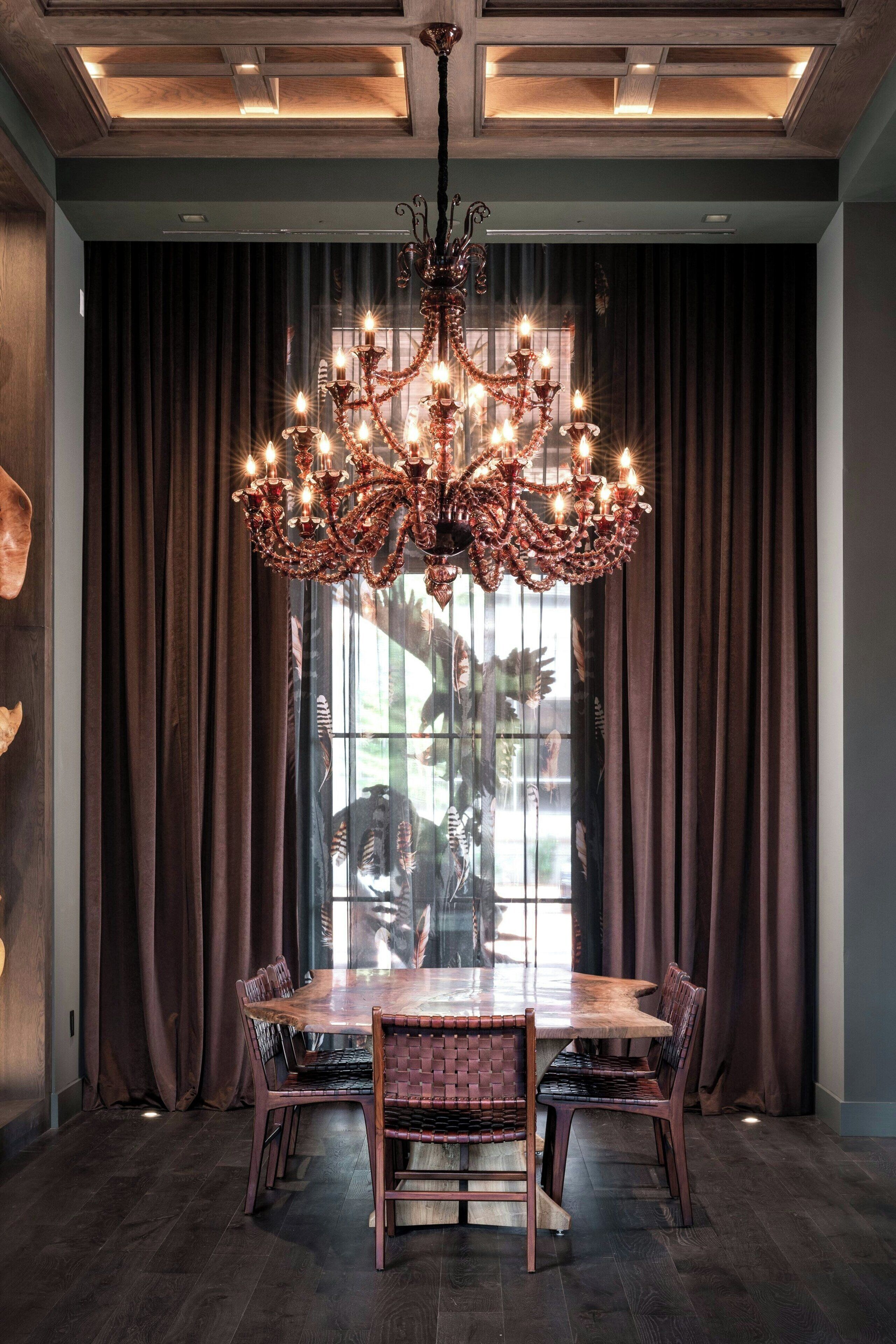 A dining area with a large wooden table and chairs, a chandelier, and dark curtains.