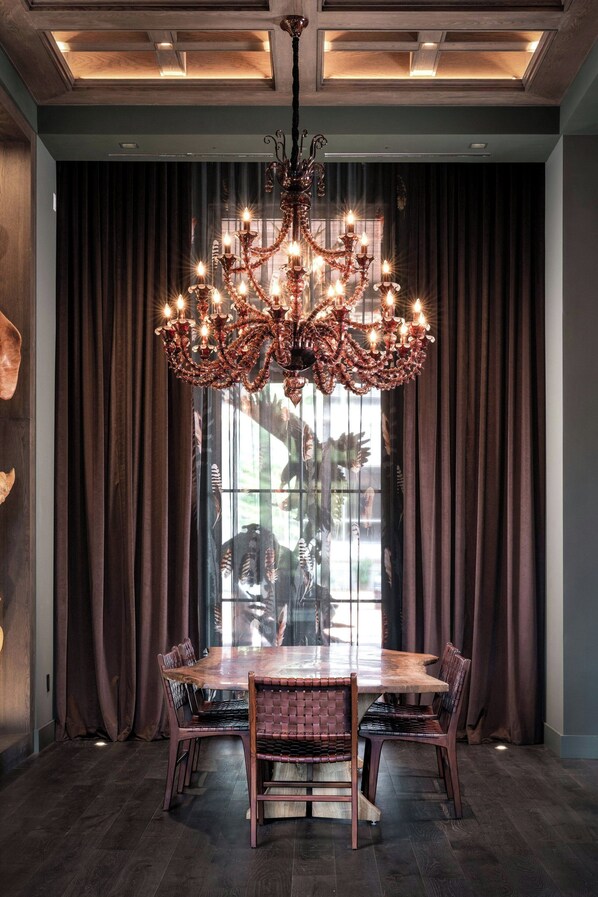 Un espace repas avec une grande table et des chaises en bois, un lustre et des rideaux sombres.