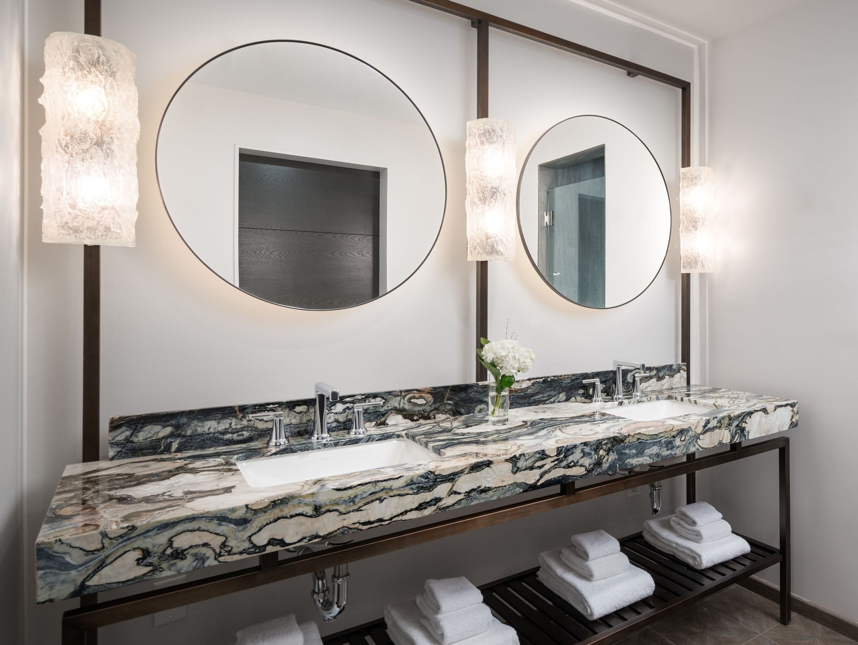 A bathroom with two sinks, a marble countertop, and a mirror with lights.