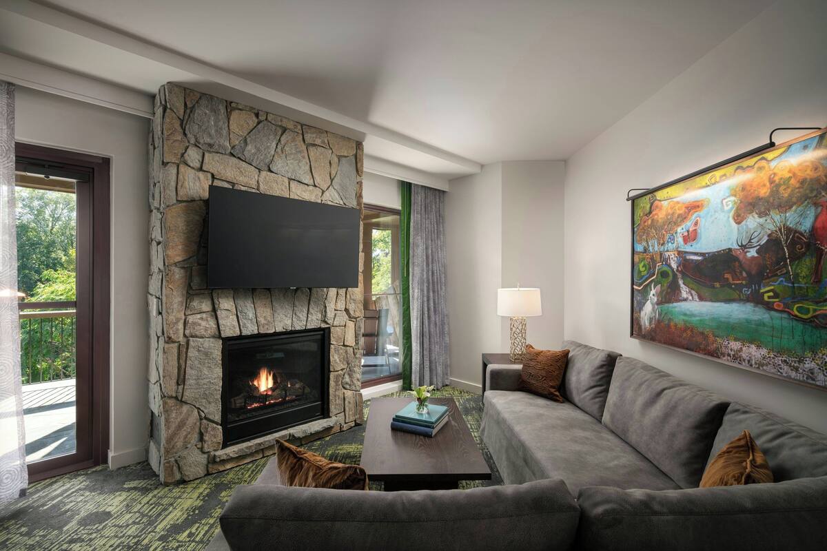 A living room with a stone fireplace, a flat-screen TV, a sofa, and a painting on the wall.
