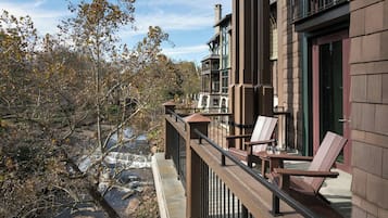 A balcony with wooden railings, a stone ledge, and two wooden chairs.