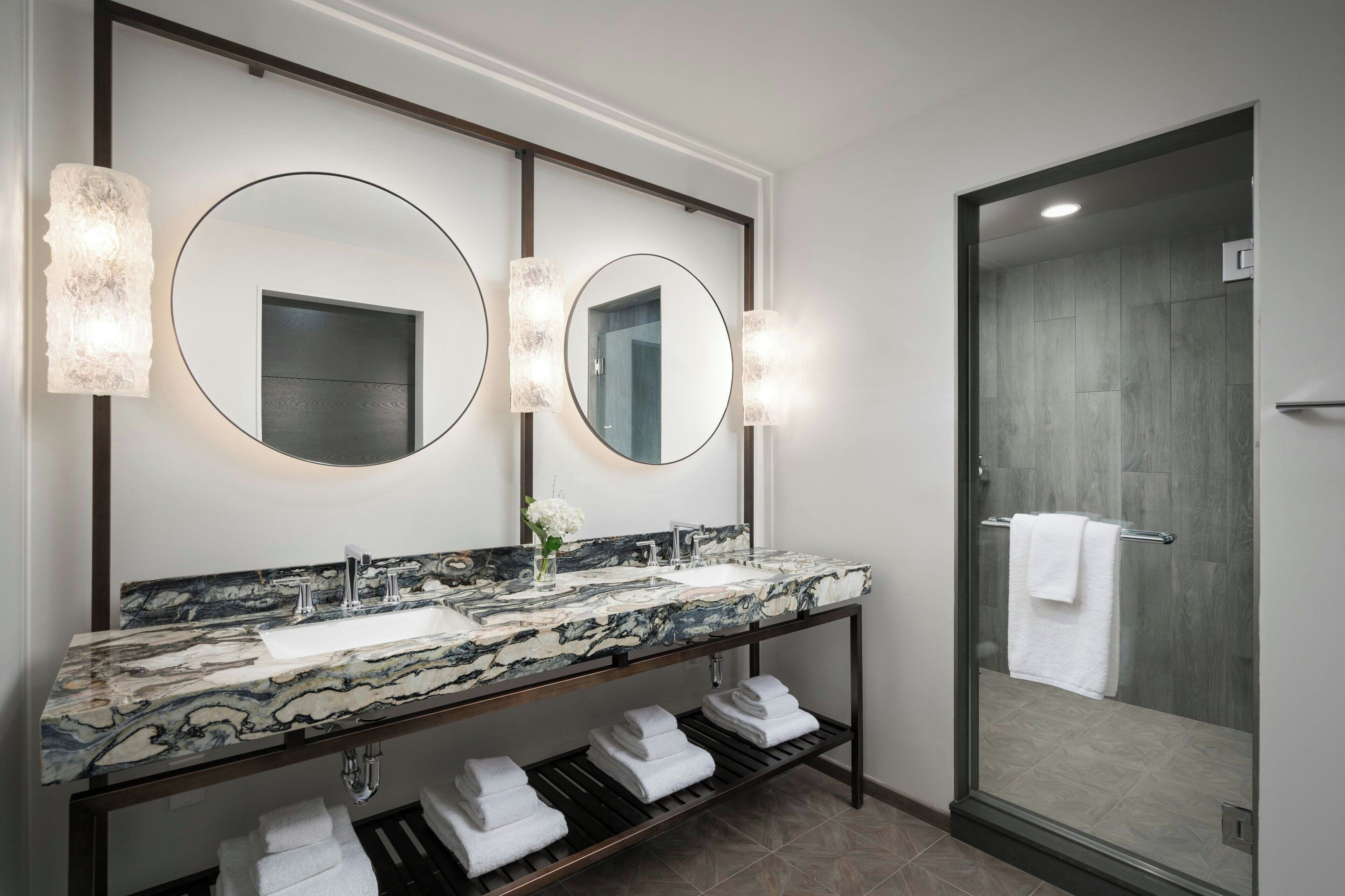 A modern bathroom with a marble sink, double mirrors, and a glass shower enclosure.