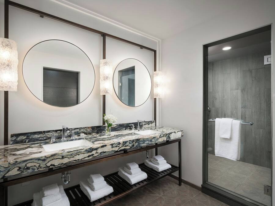 A modern bathroom with a marble sink, double mirrors, and a glass shower enclosure.