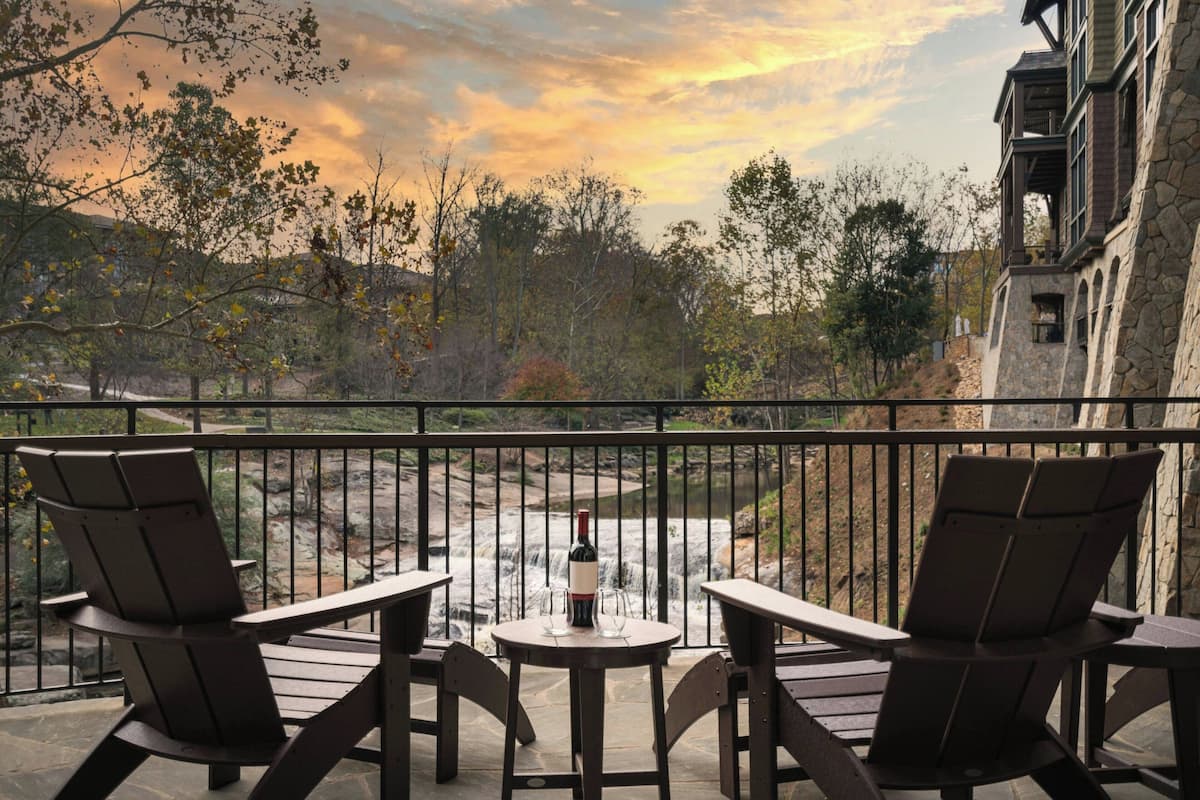 A balcony with two Adirondack chairs, a small round table, and a bottle of wine.