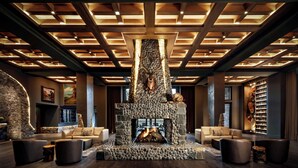 A modern interior with a stone fireplace, leather sofas, and a wooden ceiling.