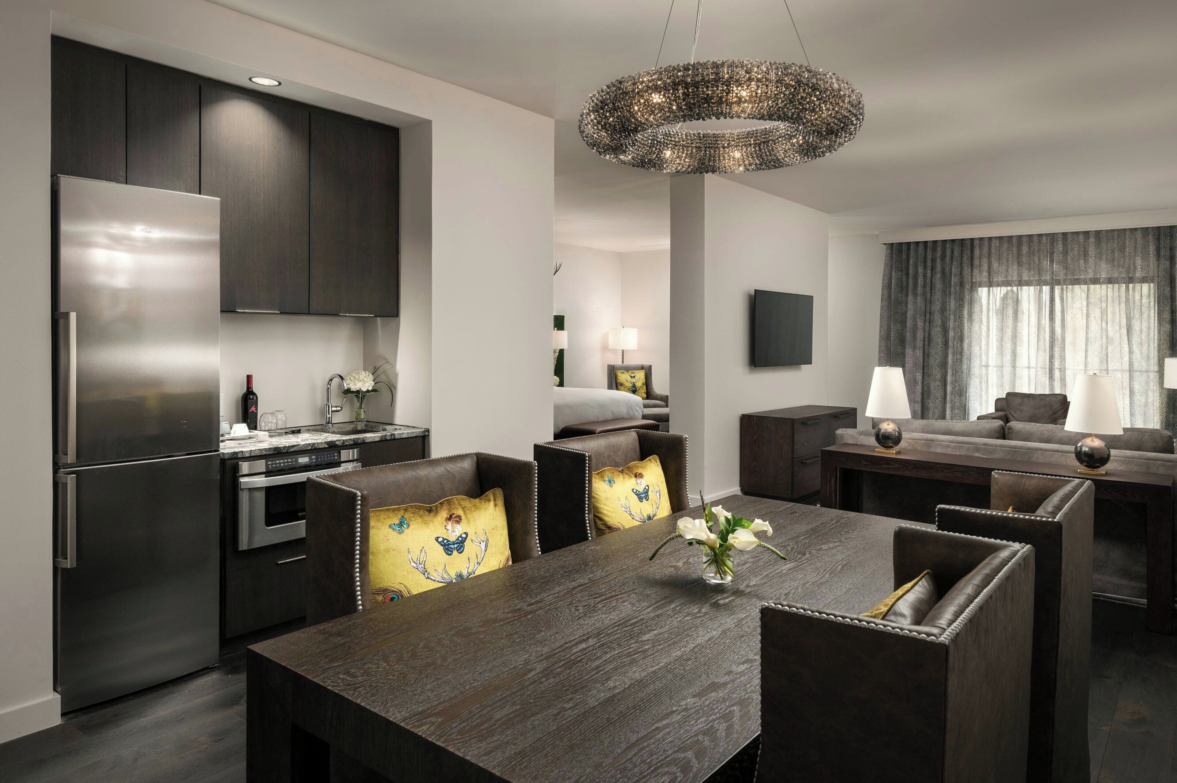 Eine moderne Küche mit dunklen Schränken, einem Edelstahlkühlschrank und einem Essbereich mit einem dunklen Holztisch und Ledersesseln.