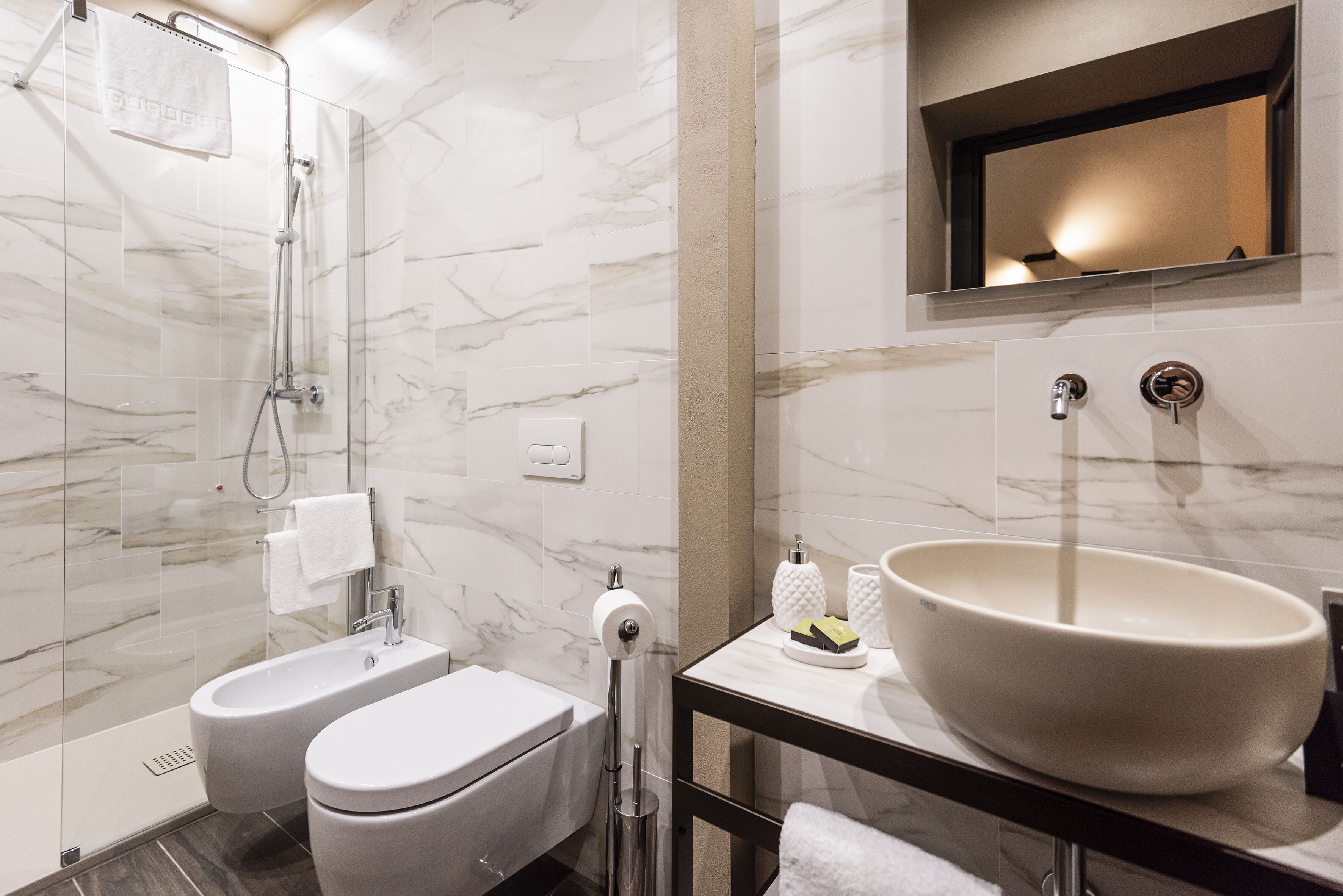 Un baño moderno con ducha envuelta en vidrio, un lavamanos grande tipo pedestal y pared cubierta de azulejos de mármol.