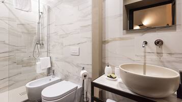 Un baño moderno con ducha envuelta en vidrio, un lavamanos grande tipo pedestal y pared cubierta de azulejos de mármol.