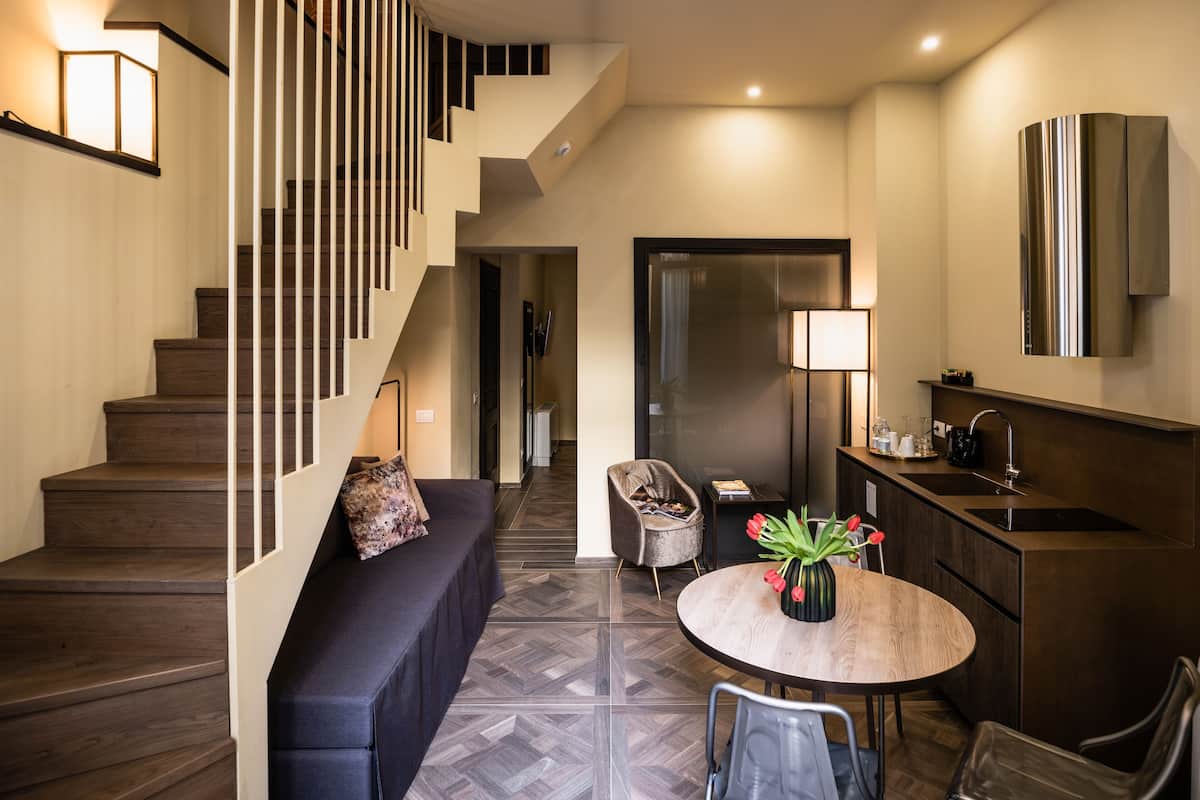 A modern interior with a staircase, a sofa, a round table with a vase of flowers, and a kitchen area.