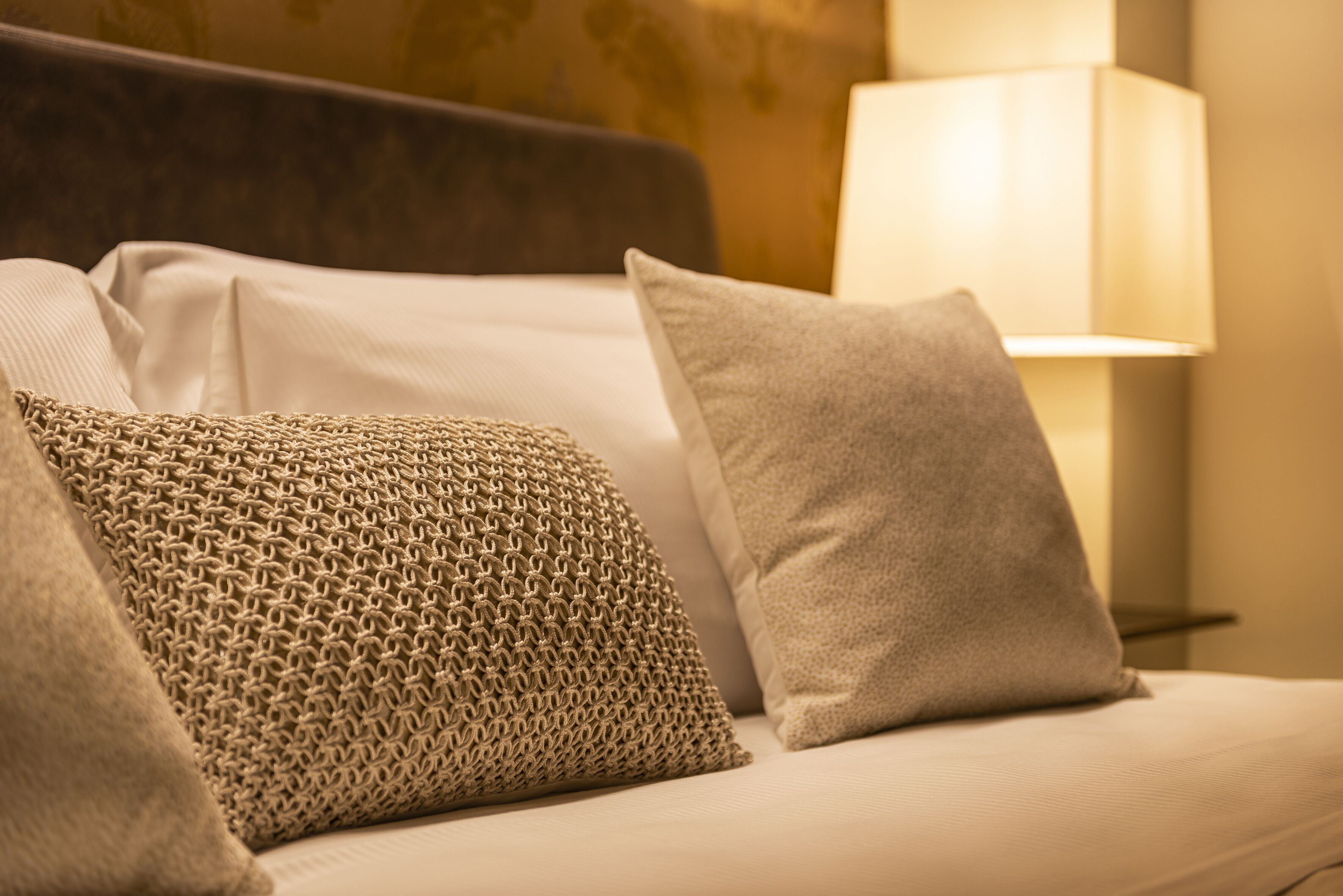 A sofa with patterned and plain cushions, a lamp, and a textured wall.