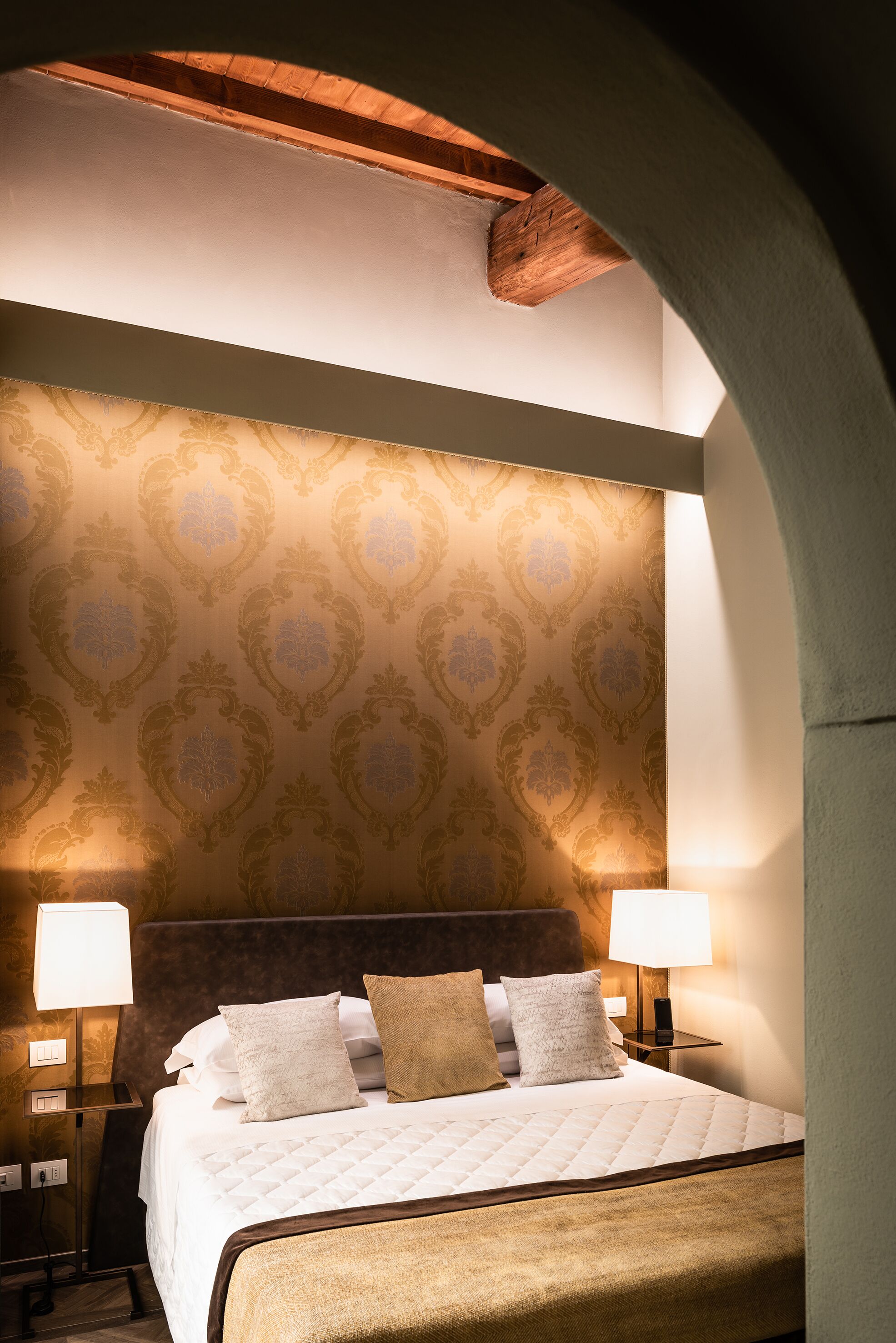 A hotel room with a large bed, two bedside lamps, and a patterned wallpaper.