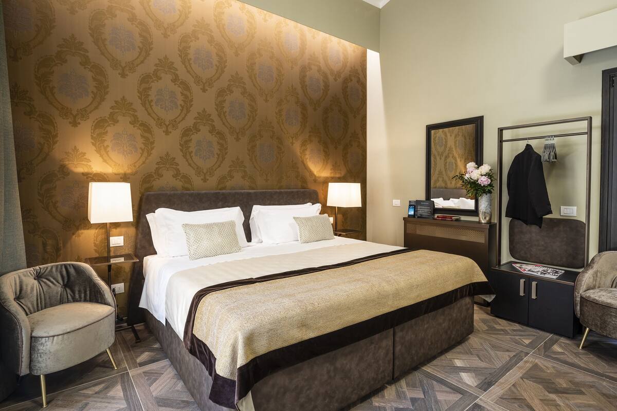 A hotel room with a large bed, two bedside lamps, a nightstand, a dresser, a chair, and a mirror.