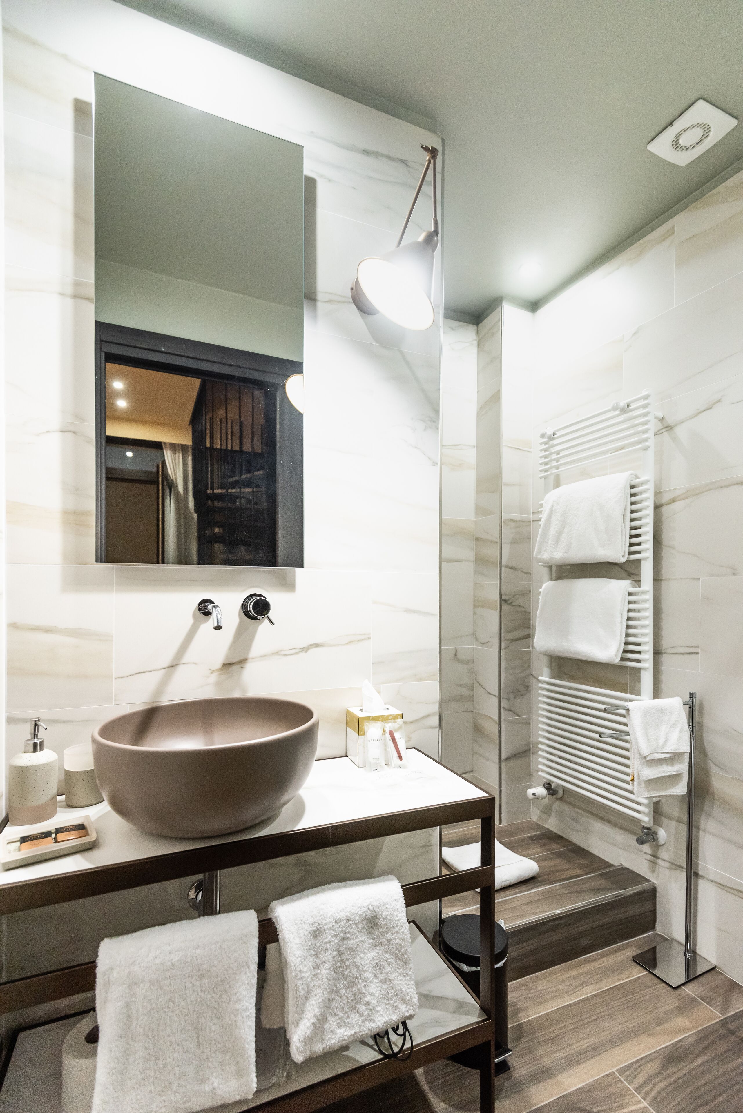 A modern bathroom with a large vessel sink, a mirror, a towel rack, and a shower area.