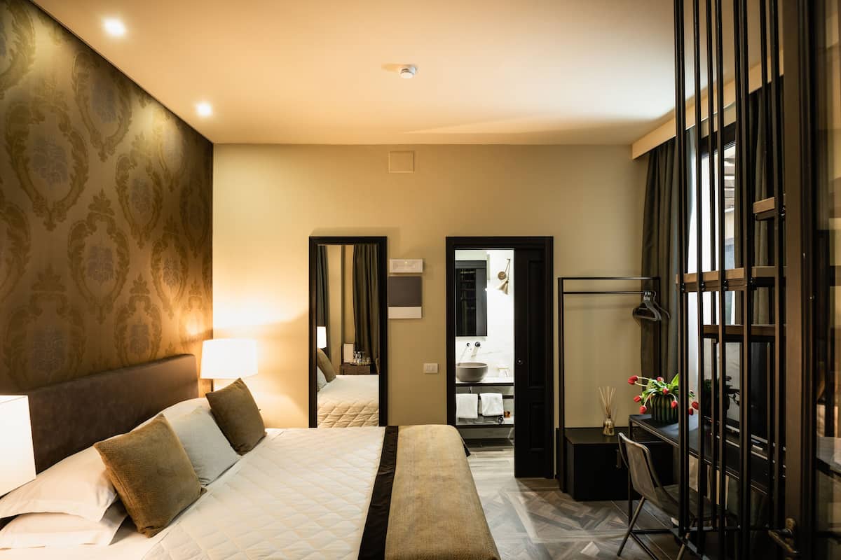 A hotel room with a large bed, a desk, and a mirror.