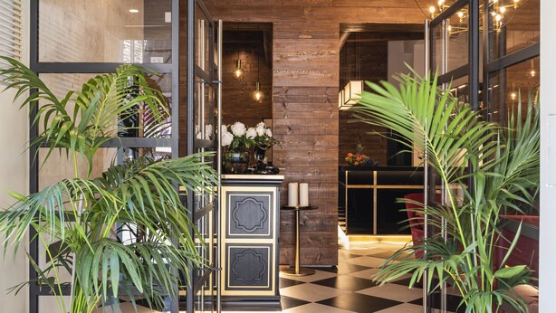 L’entrée d’un hôtel, avec un sol à carreaux, des plantes en pot et une enseigne indiquant « CORTE GUELFA ».