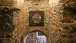 Un arc en pierre mène à un espace dédié à la salle à manger, où se trouvent une table et des chaises, le tout étant entouré de murs en pierre et agrémenté d’un élément décoratif en métal.