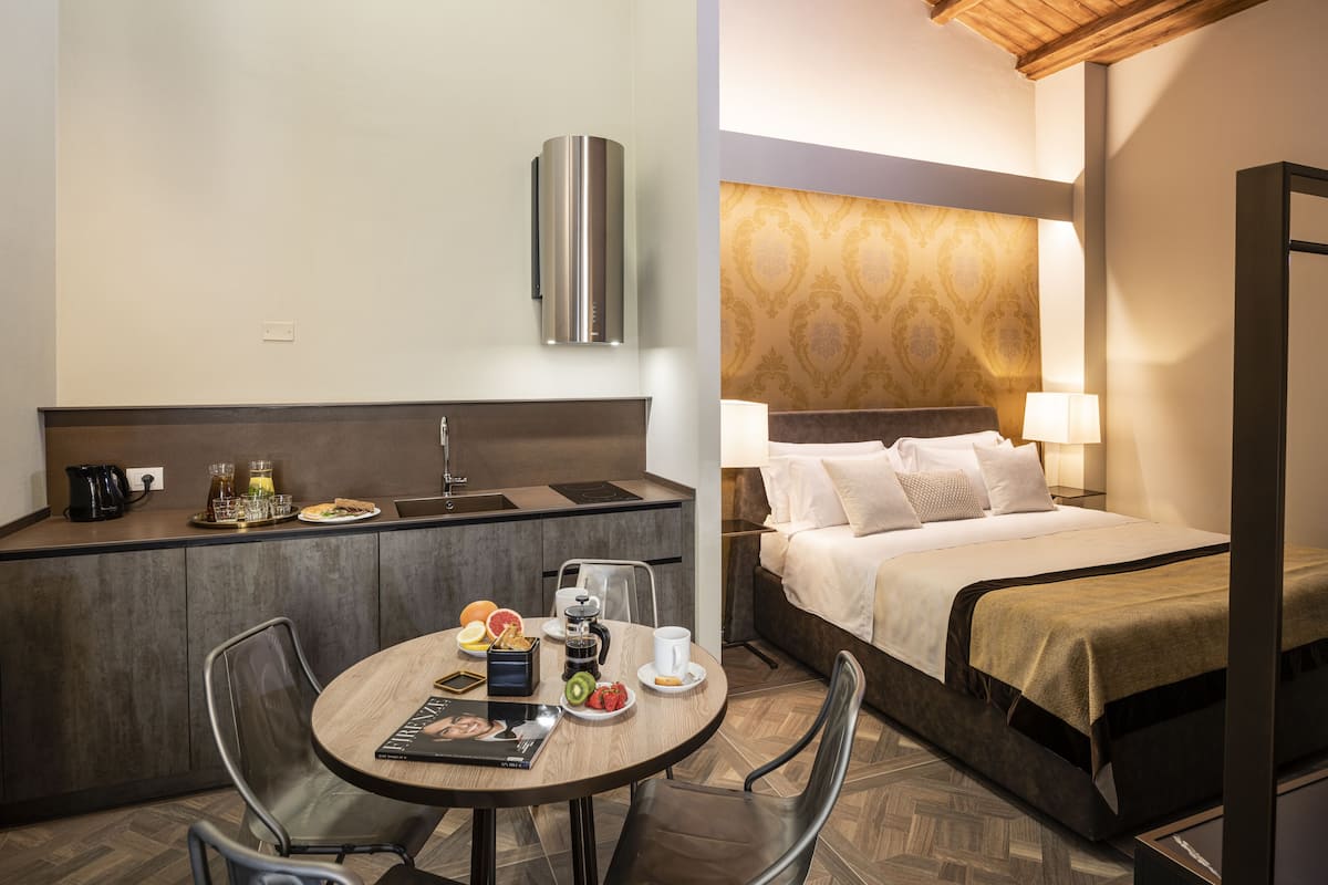 A hotel room with a kitchenette, a dining area with a table and chairs, and a bed with a headboard.