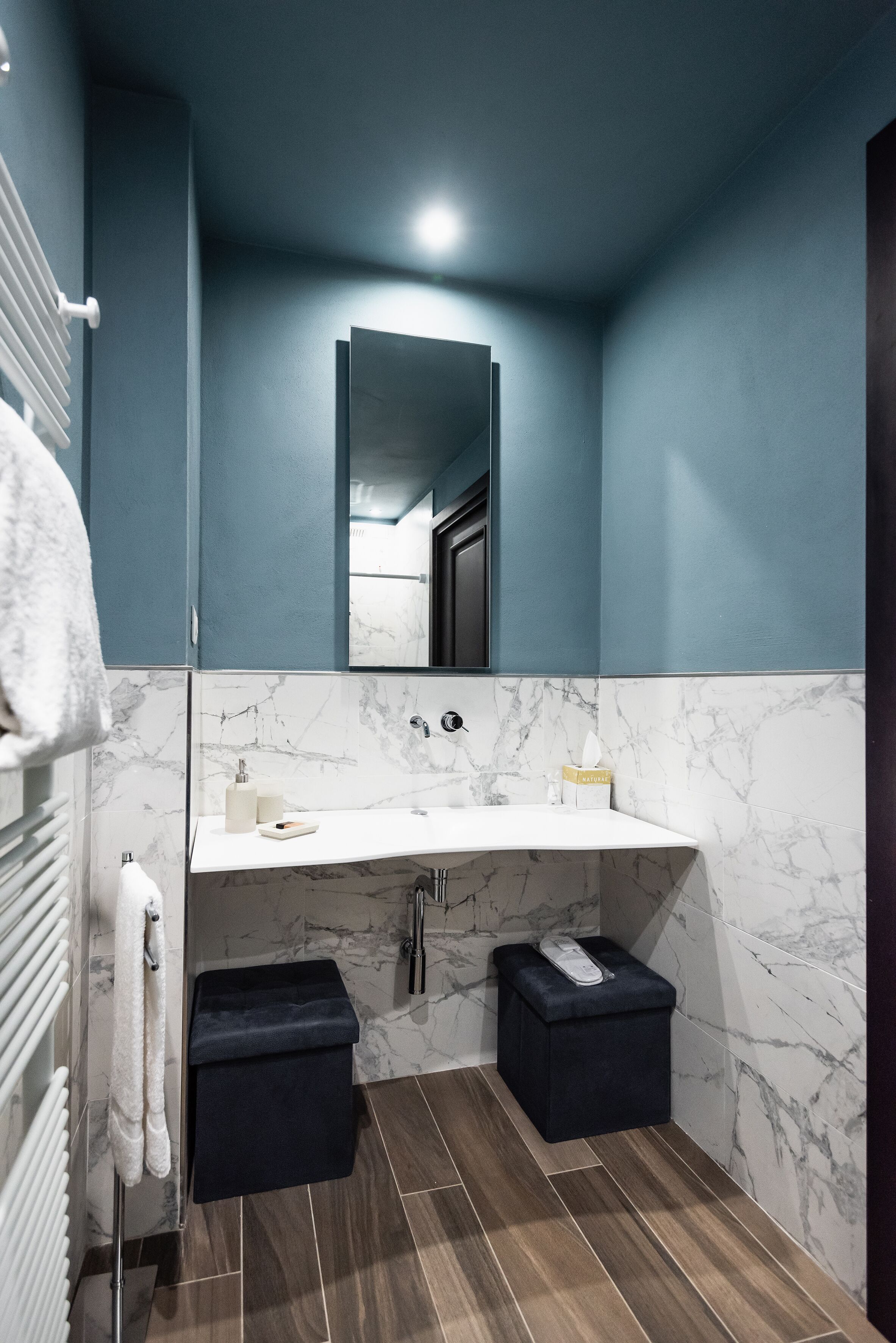A bathroom with a white marble sink, dark blue walls, and a mirror above the sink.