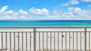 Uitzicht op het strand vanaf een balkon, met een heldere lucht, een zandstrand en een pier in de verte.
