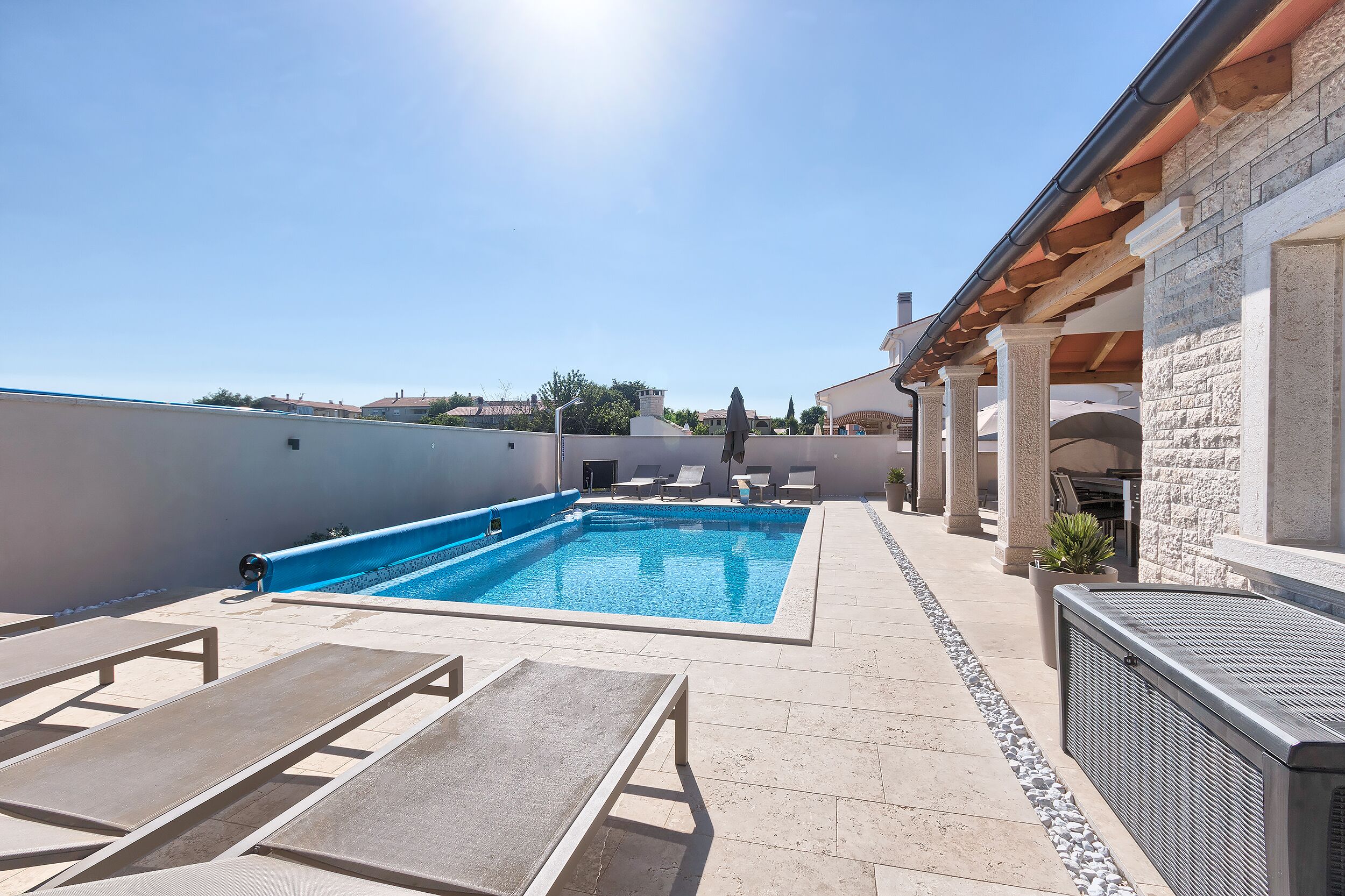 Une piscine sur le toit, agrémentée de chaises longues, un bâtiment en pierre et un ciel dégagé.