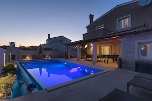 Una piscina con bordo piastrellato, un patio coperto con posti a sedere all'aperto e un muro in pietra.