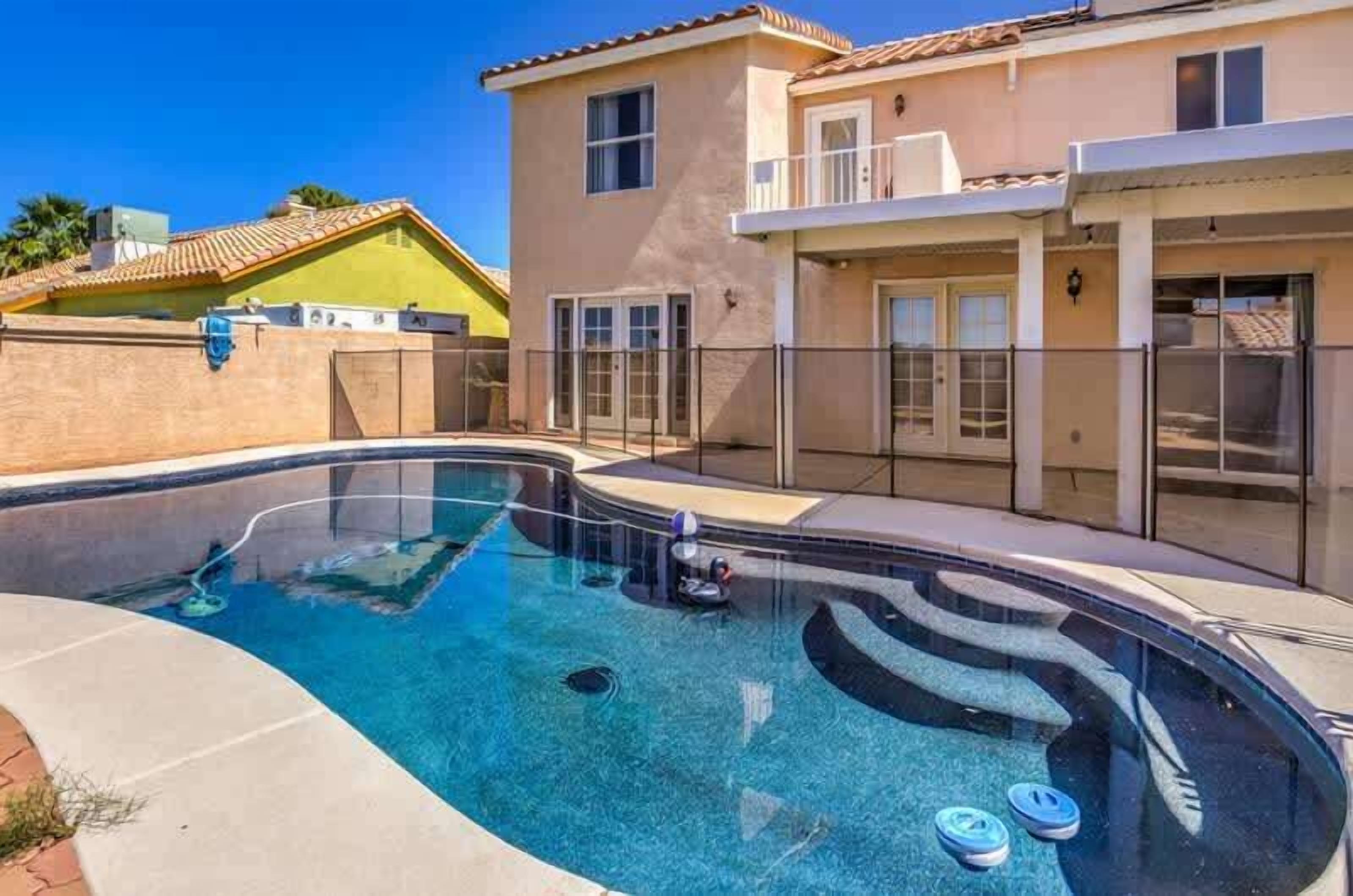 Une piscine à l’eau d  ’un bleu cristallin, entourée d’une maison dotée d’un balcon et d’un patio couvert.