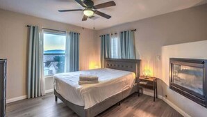 Ein Schlafzimmer mit Bett, Deckenventilator, Nachttisch, Fenster mit Vorhängen und einem gerahmten Bild an der Wand.