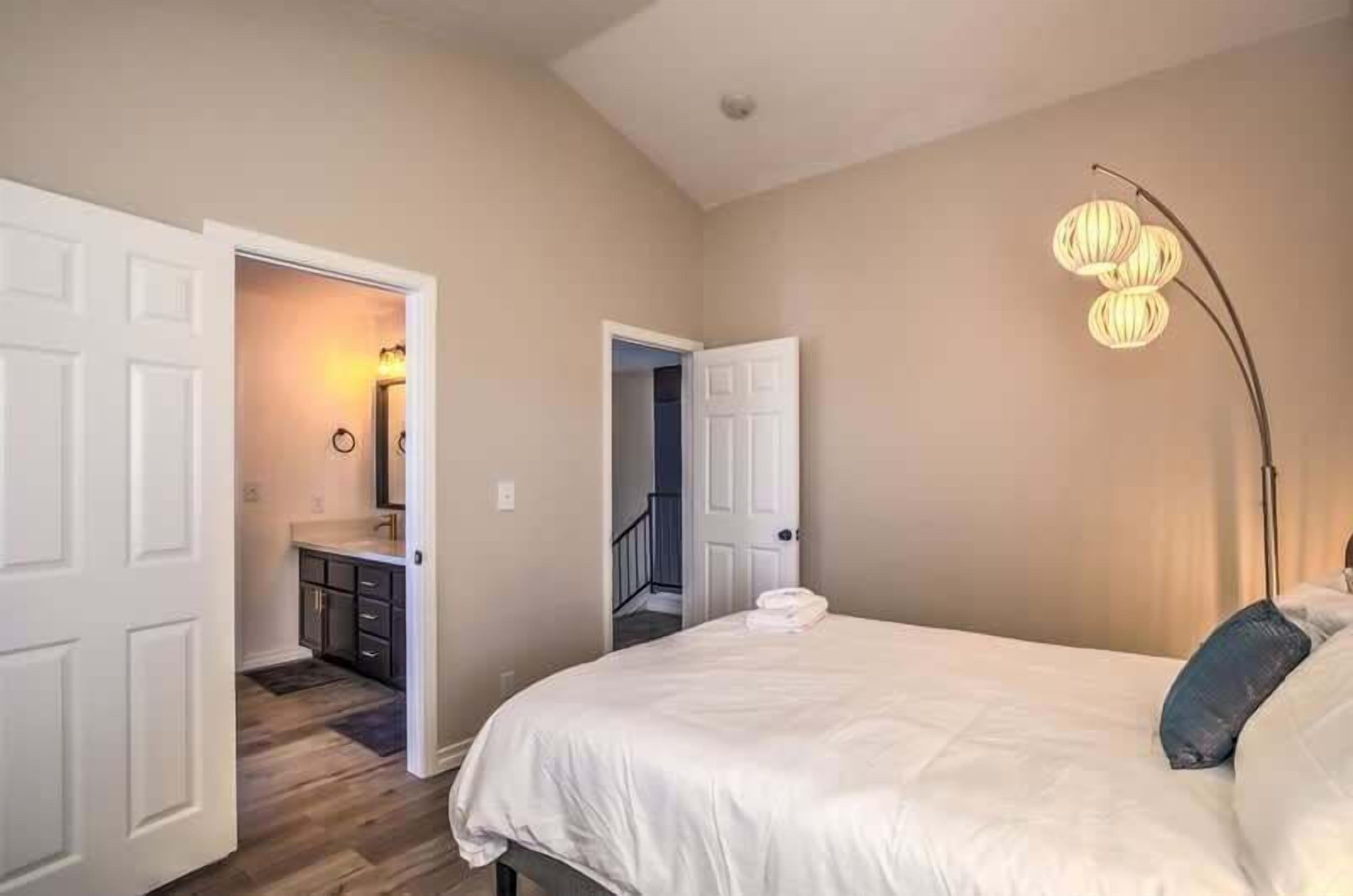 A bedroom with a bed, a nightstand, a lamp, and a door leading to a bathroom.