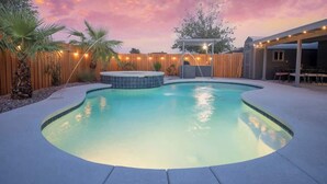 A backyard with a swimming pool, a hot tub, and a covered patio area.