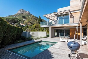 Ett modernt hus med en swimmingpool, en grillplats och utsikt över ett berg.