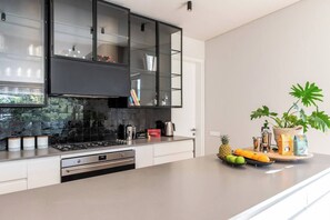 A modern kitchen with a gas stove, stainless steel appliances, and a large island with fruits and coffee equipment.