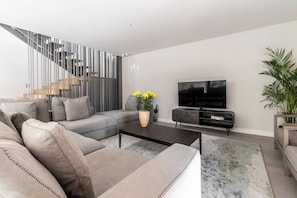A modern living room with a sectional sofa, a coffee table, a TV, and a staircase with a railing.
