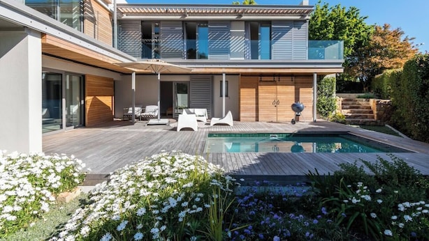 Uma casa moderna de dois andares com piscina, móveis de exterior e um jardim.