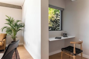A modern room with a desk, a chair, a potted plant, and a window with a view of greenery.