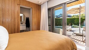 Quarto com cama, banheiro e porta de vidro deslizante que dá para uma área de varanda externa.