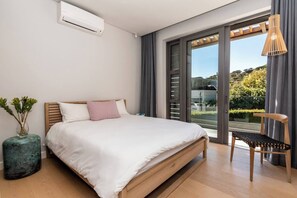 Ein modernes Schlafzimmer mit einem großen Bett, einem Sessel, einem Fenster mit Aussicht und einer Klimaanlage.