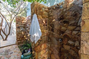 Eine Steinsäule mit einer Dusche, ein Handtuch darüber und ein Baum im Hintergrund.