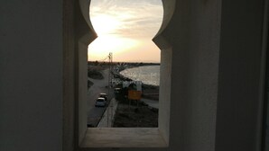 A view through a window with an arch, overlooking a coastal road with vehicles and a signboard. - APARTMENT IN HERGLA SEA VIEW (Hergla)
