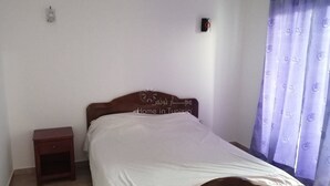 A bedroom with a bed, a nightstand, a wall-mounted light, and a curtain. - APARTMENT IN HERGLA SEA VIEW (Hergla)
