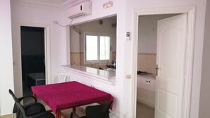 A small dining area with a table and chairs, a kitchen visible through an open door, and a window with blinds. - APARTMENT IN HERGLA SEA VIEW (Hergla)